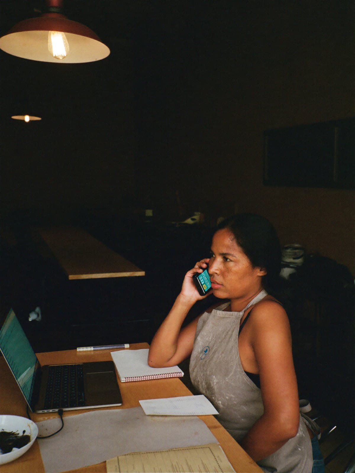 Someone doing the paperwork at a bench after close, phone to their ear.